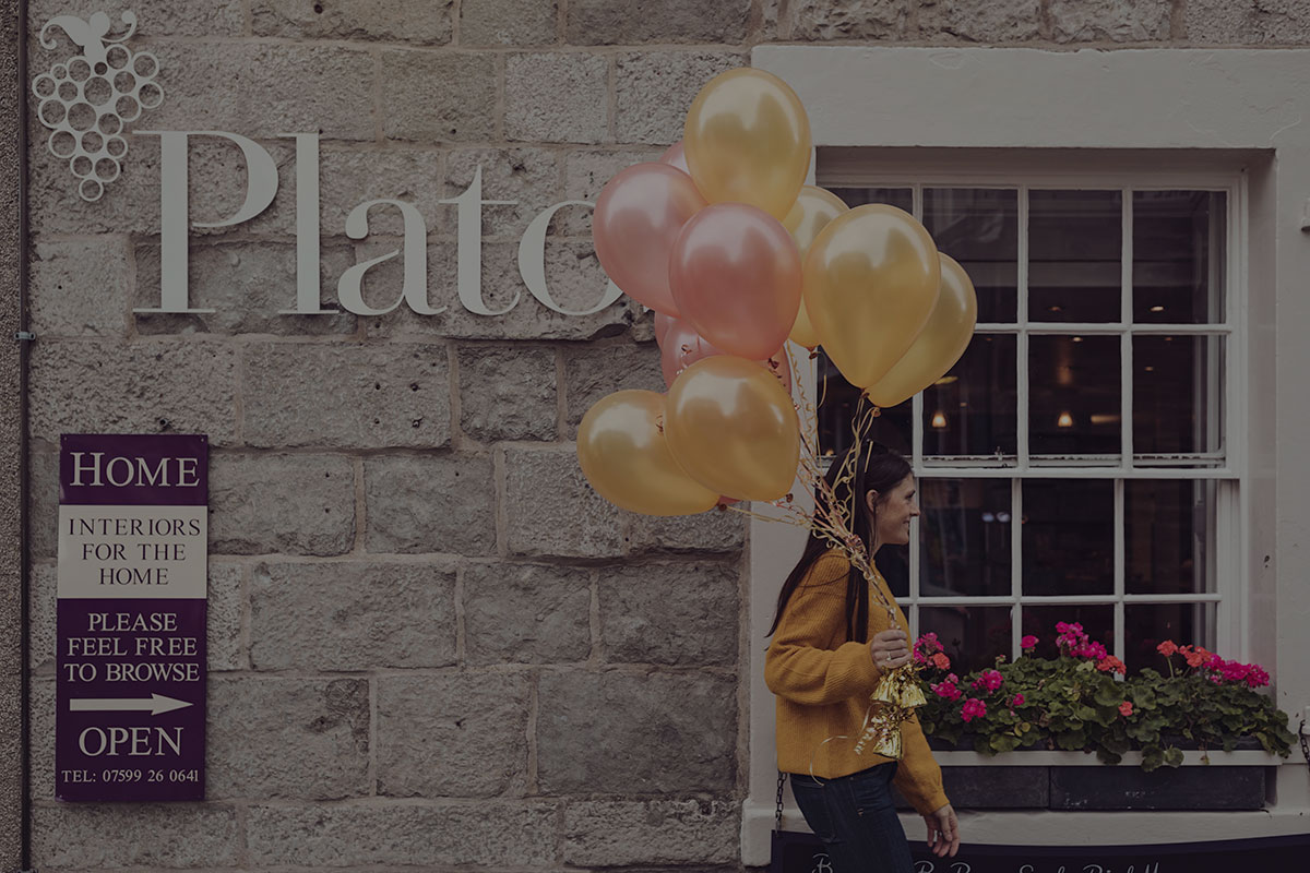 Lady walking outside Plato's with a bunch of balloons