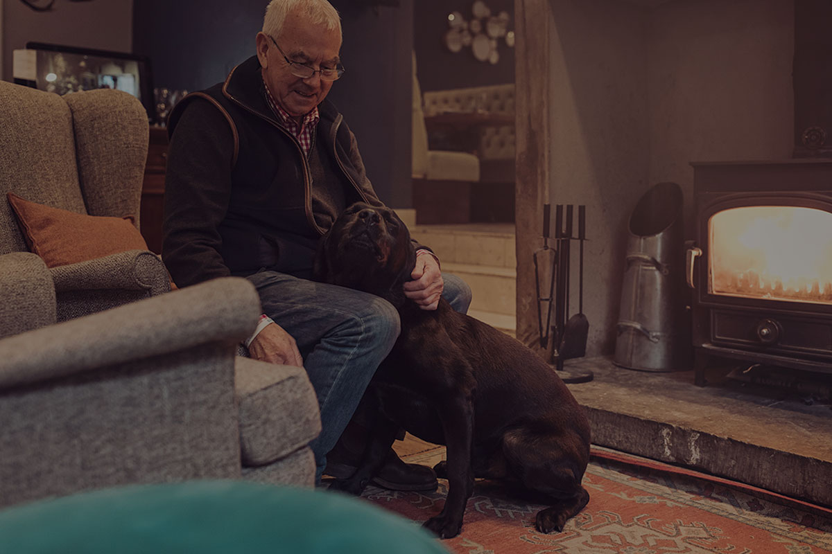 Barry Robinson sat by the fire with a Black Labrador